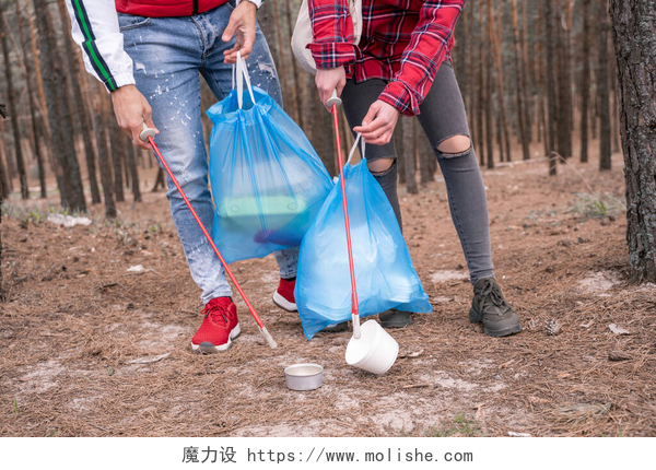 一个男人和一个女人在捡垃圾带垃圾袋的夫妇在森林里用拾拾工具捡拾垃圾的剪影 